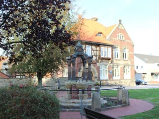 Ortsmitte Rehburg Historischer Brunnen in Rehburgs Ortsmitte, flankiert von Bäumen und einem stattlichen Fachwerkhaus.