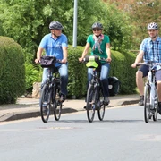 Radfahrer Drei Radfahrer und ein Kind in einem Fahrradanhänger fahren entspannt auf einer Wohnstraße entlang.
