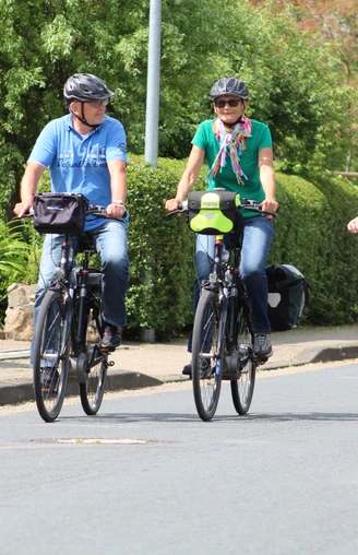 Radfahrer Drei Radfahrer und ein Kind in einem Fahrradanhänger fahren entspannt auf einer Wohnstraße entlang.
