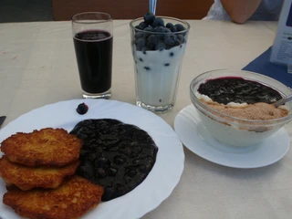 Blaubeergerichte Drei Teller mit Blaubeerpfannkuchen, Blaubeerpudding und Buttermilch mit Blaubeeren auf einem Tisch.