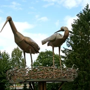Störche im Kreisel Zwei metallene Storchfiguren stehen auf einem kunstvoll gestalteten Nest inmitten eines Kreisverkehrs.
