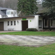Gästepavillon in der Oldendorfer Schweiz Pavillon in bewaldeter Umgebung mit Schachbrettplatz im Vordergrund, umringt von Bäumen und Gebäuden.