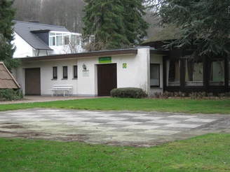 Gästepavillon in der Oldendorfer Schweiz Pavillon in bewaldeter Umgebung mit Schachbrettplatz im Vordergrund, umringt von Bäumen und Gebäuden.
