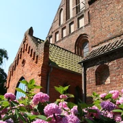 Kirche St. Cosmae und Damiani  Backsteinkirche mit hübschen Dachfirsten und Rosen im Vordergrund unter klarem blauem Himmel.