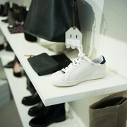 THE WANTS SHOES Weißer Sneaker auf einem Display, umgeben von verschiedenen Accessoires und Schuhen in neutralen Tönen.White sneaker on a display, surrounded by various accessories and shoes in neutral tones.