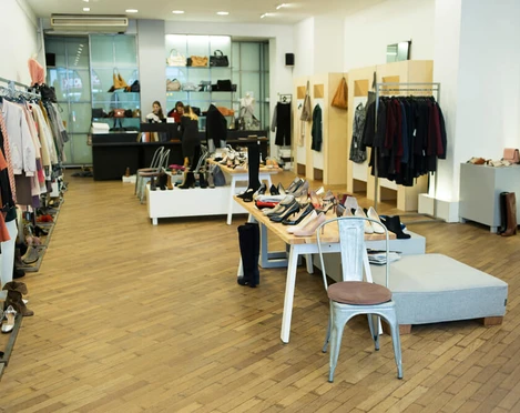 PREGO Das Bild zeigt ein modernes Geschäft mit stilvoller Kleidung, Accessoires und Schuhen, die ordentlich auf hölzernen Regalen und Tischen präsentiert sind. Der Verkaufsraum ist hell beleuchtet, mit klaren Linien und einer einladenden Atmosphäre.The image shows a modern store with stylish clothing, accessories and shoes neatly displayed on wooden shelves and tables. The salesroom is brightly lit, with clean lines and a welcoming atmosphere.