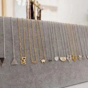 APRICOT room Eine Auswahl zarter Halsketten mit unterschiedlichen Anhängern hängt auf einer grauen Präsentationsfläche.A selection of delicate necklaces with different pendants hangs on a gray display area.