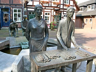 Spargelbrunnen Nienburg Bronzestatue einer Spargelerntetruppe in Nienburg, die stolz den Nienburger Spargel präsentiert.