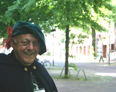 Ein älterer Mann in historischer Kleidung lächelt bei sonnigem Wetter in einem Park in Nienburg.