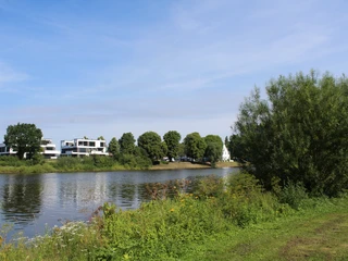 Weser Flusslauf der Weser mit grünen Ufern, modernen Gebäuden und einem Kirchturm im Hintergrund.