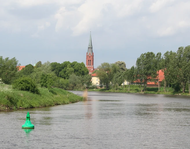 Die Weser schlängelt sich durch eine grüne Landschaft bei Nienburg; ein Kirchturm ragt im Hintergrund empor.
