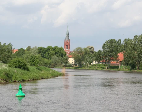 Weser bei Nienburg Die Weser schlängelt sich durch eine grüne Landschaft bei Nienburg; ein Kirchturm ragt im Hintergrund empor.