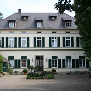 Rittergut Schlüsselburg Herrenhaus mit zwei Stockwerken, grünen Fensterläden, Kiesweg und Garten, umgeben von Bäumen.