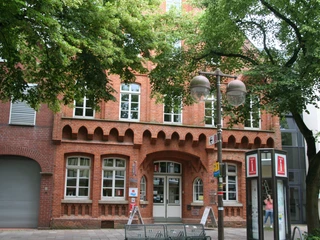 Tourist-Information Nienburg Historisches Backsteingebäude in Nienburg mit Tourist-Information unter Bäumen und umliegenden Geschäften.