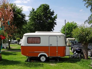 Camping Berger Ein farbenfroher Wohnwagen steht auf einem grünen Rasen zwischen zwei Bäumen.A colorful caravan stands on a green lawn between two trees.