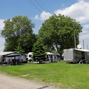 Camping Berger Sorgfältig gepflegte Campingwiese mit Wohnwagen unter Bäumen und strahlend blauem Himmel bei Camping Berger.Carefully maintained camping meadow with caravans under trees and a bright blue sky at Camping Berger.