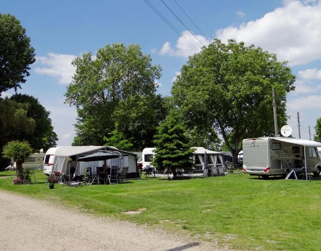 Camping Berger Sorgfältig gepflegte Campingwiese mit Wohnwagen unter Bäumen und strahlend blauem Himmel bei Camping Berger.Carefully maintained camping meadow with caravans under trees and a bright blue sky at Camping Berger.