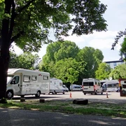 Motorhome park Wohnmobile parken unter schattigen Bäumen, im Hintergrund grünes Laub und strahlend blauer Himmel.Motorhomes parked under shady trees, green foliage and a bright blue sky in the background.