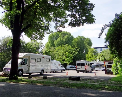 Motorhome park Wohnmobile parken unter schattigen Bäumen, im Hintergrund grünes Laub und strahlend blauer Himmel.Motorhomes parked under shady trees, green foliage and a bright blue sky in the background.