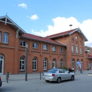 Bahnhof Kirchweyhe Backstein-Gebäude mit rotem Dach und Rundbogenfenstern, parkende Autos vor blauem Himmel.