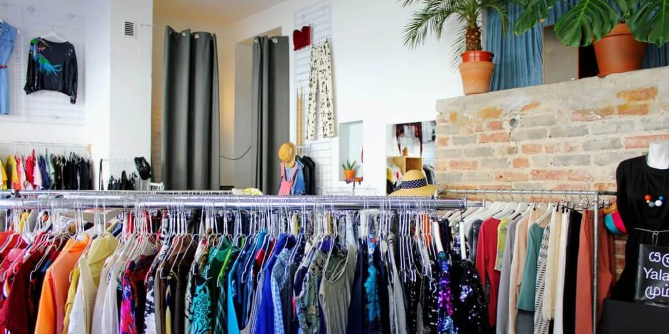Kleiderei Innenansicht einer Boutique mit bunter Kleidung auf Kleiderständern und dekorativen Pflanzen.Interior view of a boutique with colorful clothes on clothes racks and decorative plants.