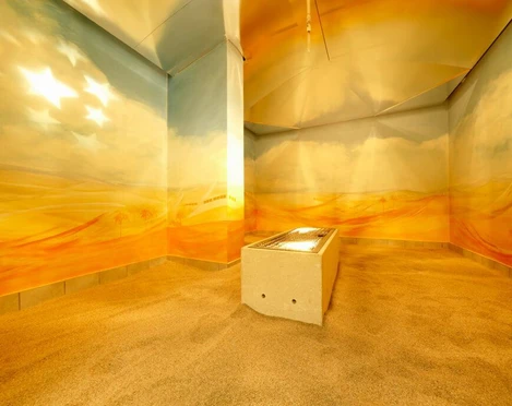 Agrippa bath In einem warmen, sandfarbenen Raum steht eine beleuchtete Liege, umgeben von sanften Wandmalereien.An illuminated lounger stands in a warm, sand-colored room, surrounded by soft wall paintings.