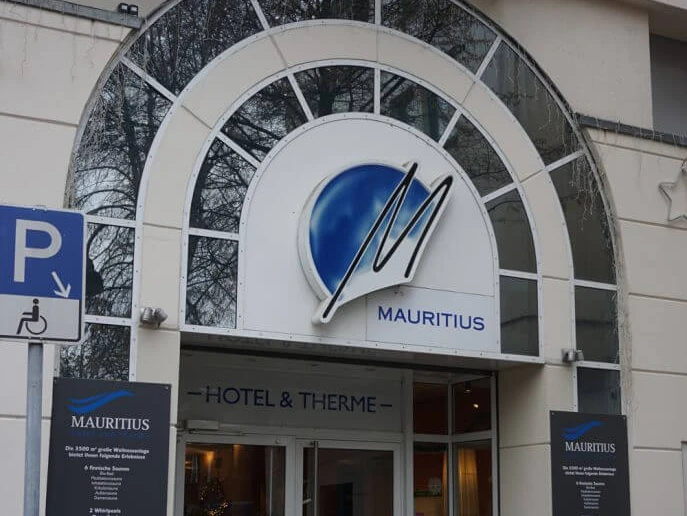 Mauritius Hotel and Spa Eingang zu Mauritius Hotel & Therme mit überdachtem Bogen und markantem blauen Logo.Entrance to Mauritius Hotel & Therme with covered arch and striking blue logo.
