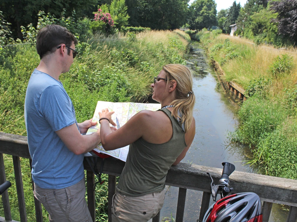Radfahren Zwei Radfahrer stehen auf einer Brücke und betrachten eine Karte. Ein Fluss fließt darunter.