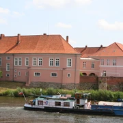 Grafenschloss zu Hoya Altes Grafenschloss an der Weser, rosafarben, umgeben von Bäumen und Fluss, im ruhigen Tageslicht.