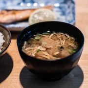 Restaurant Kintaro Nahaufnahme einer kleinen schwarzen Schüssel, gefüllt mit einer Rindersuppe, daneben ein Schälchen Reis. Close-up of a small black bowl filled with beef soup, next to it a small bowl of rice.