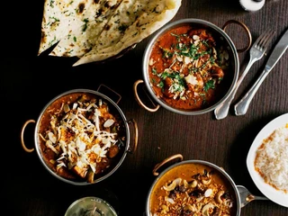 Ginti Ein Tisch gedeckt mit indischen Spezialitäten in kleinen Schüsseln dazu Reis und Naanbrot.A table set with Indian specialties in small bowls, along with rice and naan bread.