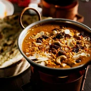 Ginti Nahaufnahme einer kleinen Metallschüssel mit Curry und Brotkorb, gefüllt mit Naanbrot.Close-up of a small metal bowl of curry and a bread basket filled with naan bread.