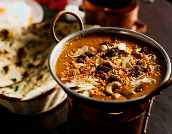Ginti Nahaufnahme einer kleinen Metallschüssel mit Curry und Brotkorb, gefüllt mit Naanbrot.Close-up of a small metal bowl of curry and a bread basket filled with naan bread.