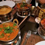 Royal Punjab Vier dampfende Curry-Gerichte in typischen indischen Servierschalen auf einem gedeckten Tisch.Four steaming curry dishes served in traditional Indian bowls, arranged on a set table.