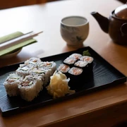 Fisch Hof Sushi Haus Sushi präsentiert auf einem schwarzen Teller. Im Hintergrund eine Kupferteekanne.Sushi presented on a black plate. In the background, a copper teapot.