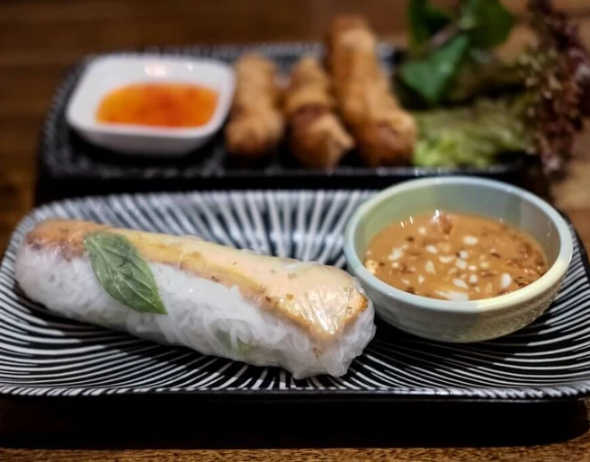 Restaurant Lua by Danny Nahaufnahme einer Sommerrolle mit einem Schälchen Erdnusssoße. Close-up of a summer roll with a small bowl of peanut sauce.