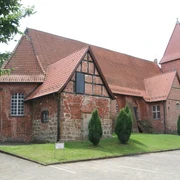Backsteinkirche mit mittelalterlichem Fachwerk und Spitzdach, umgeben von Grün und blauem Himmel.