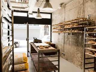 prôt Eine kleine Bäckerei mit rustikaler Backsteinwand und Regalen voller frisch gebackener Brote und Brötchen.A small bakery featuring rustic brick walls and shelves filled with freshly baked breads and rolls.