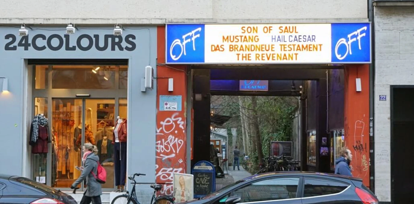 OFF Broadway Eingang des OFF-Broadway-Kinos in Köln, mit Passanten und parkenden Autos.Entrance to the OFF-Broadway cinema in Cologne, with passers-by and parked cars.