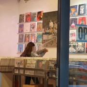 Parallel Schallplatten Ein Schallplattenladen mit offenen Türen zeigt eine Person, die im Inneren Schallplatten durchstöbert.A record store with open doors shows a person browsing through records inside.
