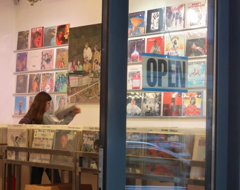 Parallel Schallplatten Ein Schallplattenladen mit offenen Türen zeigt eine Person, die im Inneren Schallplatten durchstöbert.A record store with open doors shows a person browsing through records inside.