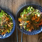 Poke Makai Zwei blaue, dekorative Schalen mit üppigen Poke-Gerichten, verziert mit Frühlingszwiebeln, Nori und Sesam.Two blue decorative bowls filled generously with poke dishes, garnished with spring onions, nori, and sesame seeds.