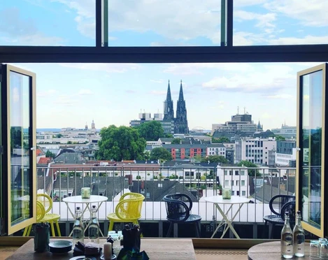 Restaurant Neni Offene Fensterfront mit urbanem Panoramablick, im Zentrum der Kölner Dom majestätisch am Horizont.Open window front with urban panoramic view, with Cologne Cathedral majestically rising on the horizon in the centre.