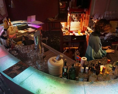 TURISTARAMA Ein eleganter Barbereich mit bunter Beleuchtung zeigt eine Person bei der Arbeit an einem Laptop.An elegant bar area with colorful lighting shows a person working on a laptop.