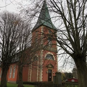 Kirche im Dorf Intschede, umgeben von kahlen Bäumen im Herbst, mit markantem grünen Kirchturm.