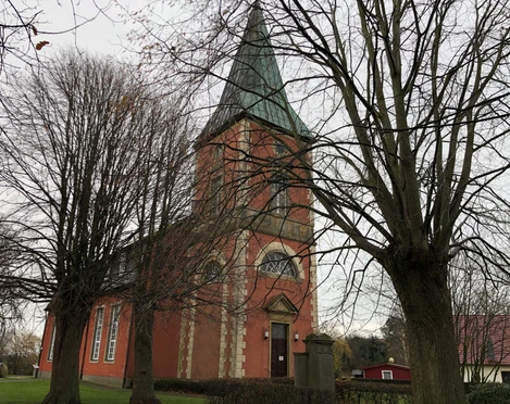 Kirche im Dorf Intschede, umgeben von kahlen Bäumen im Herbst, mit markantem grünen Kirchturm.