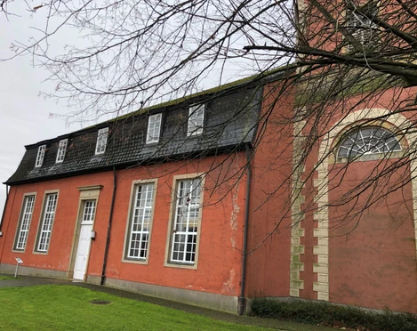 Backsteinkirche in Intschede mit großen weißen Fenstern und einer Backsteinfassade an trübem Tag.