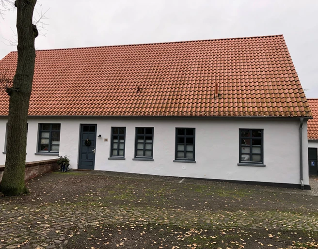 Küsterhaus Daverden Ein einstöckiges Haus mit roten Ziegeln und weißen Wänden, umgeben von einer steinernen Terrasse.