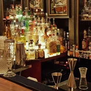 Ona Mor Cocktailbar Auf dem Bild ist eine elegante Bar mit einer Vielzahl von dekorativ beleuchteten Spirituosenflaschen, kunstvoll gestalteten Gläsern und Barutensilien auf einem edlen Holztresen zu sehen, was eine gemütliche und stilvolle Atmosphäre vermittelt.The image shows an elegant bar with a variety of decoratively lit spirits bottles, artistically designed glasses and bar utensils on a fine wooden counter, creating a cosy and stylish atmosphere.