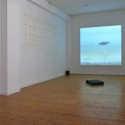 Moltkerei Werkstatt In einem minimalistisch gestalteten Raum sind auf hellem Holzboden eine Projektion und an Wänden befestigte Blätter zu sehen.In a room with a minimalist design, a projection and leaves attached to the walls can be seen on a light-colored wooden floor.